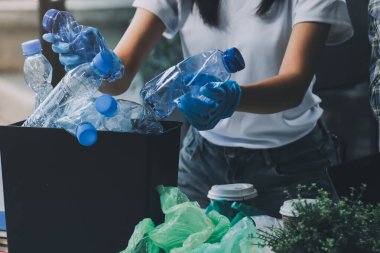 Yerden plastik atık ve şişe toplayan bir ailenin kadın ellerine yakın çekim. Eldiven giyiyorlar ve plastik kirliliğini azaltmak ve çevreyi korumak için geri dönüşüme odaklanıyorlar..