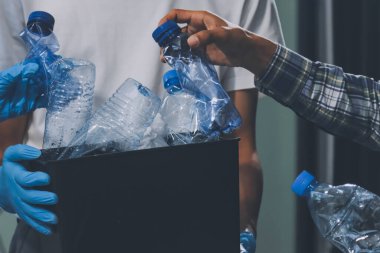 Yerden plastik atık ve şişe toplayan bir ailenin kadın ellerine yakın çekim. Eldiven giyiyorlar ve plastik kirliliğini azaltmak ve çevreyi korumak için geri dönüşüme odaklanıyorlar..