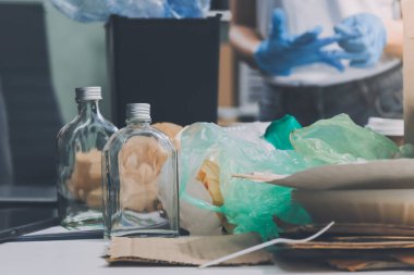 Yerden plastik atık ve şişe toplayan bir ailenin kadın ellerine yakın çekim. Eldiven giyiyorlar ve plastik kirliliğini azaltmak ve çevreyi korumak için geri dönüşüme odaklanıyorlar..