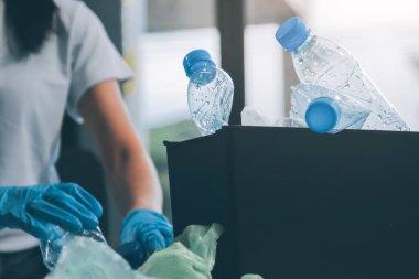 Yerden plastik atık ve şişe toplayan bir ailenin kadın ellerine yakın çekim. Eldiven giyiyorlar ve plastik kirliliğini azaltmak ve çevreyi korumak için geri dönüşüme odaklanıyorlar..