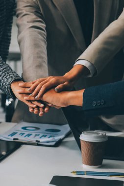 İş dünyası ekibi ellerini birleştiriyor genç iş adamlarının el ele tutuşmalarını yakından izliyorlar. İşlerin başarıya ulaşmasını sağlamak için insanlar takım olarak çalışacaklar.