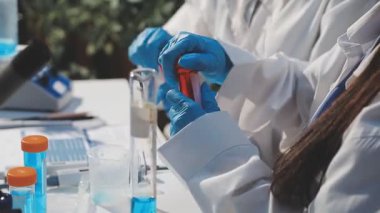 Koruyucu eldivenli kadın bilim adamı ellerinde test tüpleri tutuyor.