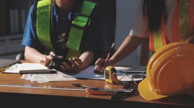 Mühendis ya da mühendis kadın mühendis ya da miğferi ya da miğferi olan işçi ya da güvenlik yeleği ile planlı ve arka planda inşaat ekipmanları olan bir bina..