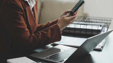 İş kadını akıllı telefon kullanıyor ve ofiste dizüstü bilgisayarla çalışıyor..