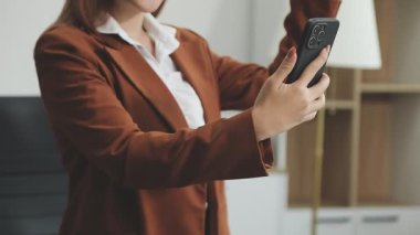 İş kadını elinde akıllı telefon tutuyor ve ofiste otururken zamanını kontrol ediyor.