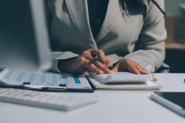 Asyalı iş kadını dizüstü bilgisayar kullanıyor ve ofiste hesap makinesi ile çalışıyor, mali raporu, iş planı yatırımını, mali analiz konseptini analiz etmeyi planlıyor..