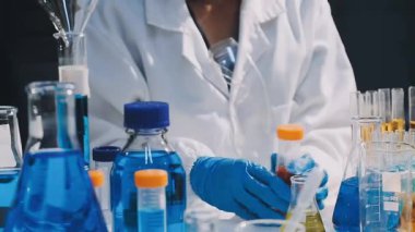 Laboratuvarda koruyucu üniforma ve eldiven giymiş kimyasal tüplü laboratuvar çalışanı.