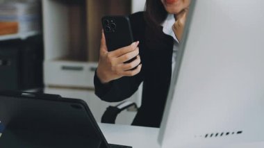 Akıllı telefon kullanan ve ofisteki dizüstü bilgisayarda yazan bir kadın..