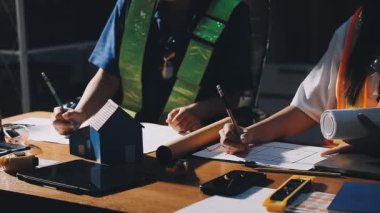 Genç Asyalı mühendis miğfer mühendisi işi kontrol ediyor ve atölyedeki masada çalışıyor..