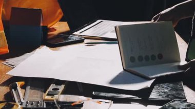 Tasarımcı projesinde çalışıyor, cep telefonunu kullanarak ahşap masa üzerinde yeni bir proje yaratıyor.