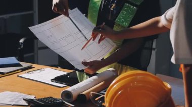 Masada dizüstü bilgisayarla çalışan mühendis veya mimar odada planlarla birlikte.