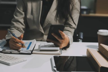 Asyalı iş kadını dizüstü bilgisayar kullanıyor ve ofiste hesap makinesi ile çalışıyor, mali raporu, iş planı yatırımını, mali analiz konseptini analiz etmeyi planlıyor..