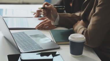 Bilgisayarları kullanarak ve modern ofisteki masaya notlar yazarak iş adamlarını kapatın. İş adamları modern çatı katında toplanıyor.