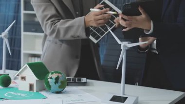 Ofis masasında rüzgar türbinleri olan takım elbiseli iş adamı ve kadın, eko enerji kavramı