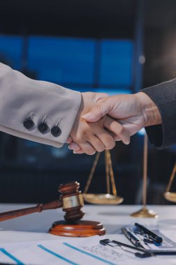 İki iş adamı bir hukuk bürosunda tartıyla ve masada tokmakla el sıkışıyor.