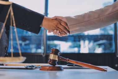 İki iş adamı bir hukuk bürosunda tartıyla ve masada tokmakla el sıkışıyor.