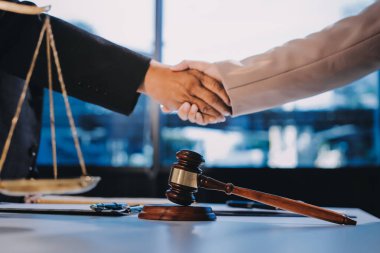 İki iş adamı bir hukuk bürosunda tartıyla ve masada tokmakla el sıkışıyor.