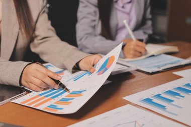 Group of confident business people point to graphs and charts to analyze market data, balance sheet, account, net profit to plan new sales strategies to increase production capacity.