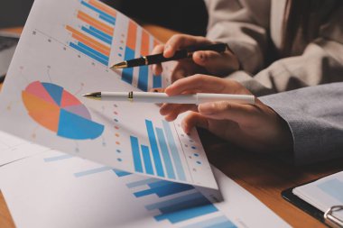 Group of confident business people point to graphs and charts to analyze market data, balance sheet, account, net profit to plan new sales strategies to increase production capacity.