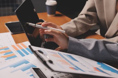 Group of confident business people point to graphs and charts to analyze market data, balance sheet, account, net profit to plan new sales strategies to increase production capacity.