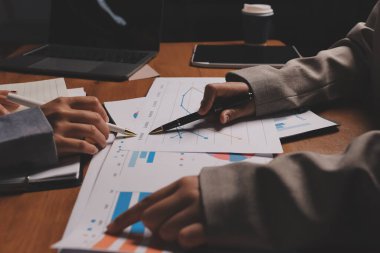 Group of confident business people point to graphs and charts to analyze market data, balance sheet, account, net profit to plan new sales strategies to increase production capacity.