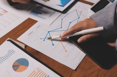 Group of confident business people point to graphs and charts to analyze market data, balance sheet, account, net profit to plan new sales strategies to increase production capacity.