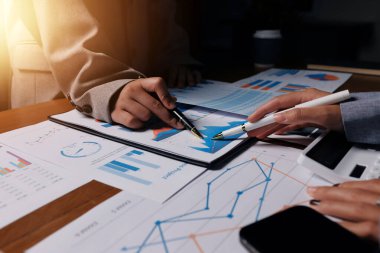 Group of confident business people point to graphs and charts to analyze market data, balance sheet, account, net profit to plan new sales strategies to increase production capacity.