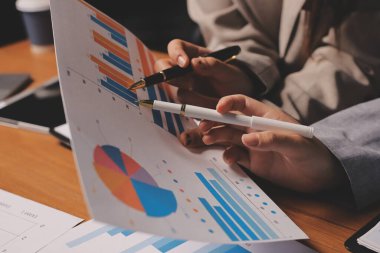 Group of confident business people point to graphs and charts to analyze market data, balance sheet, account, net profit to plan new sales strategies to increase production capacity.