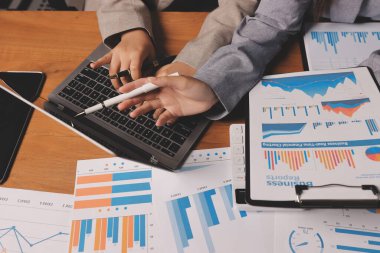 Group of confident business people point to graphs and charts to analyze market data, balance sheet, account, net profit to plan new sales strategies to increase production capacity.