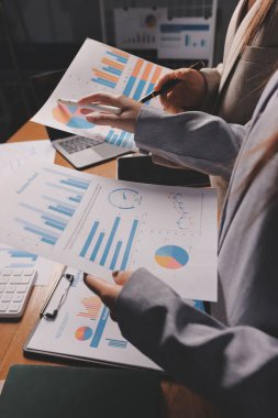 Group of confident business people point to graphs and charts to analyze market data, balance sheet, account, net profit to plan new sales strategies to increase production capacity.