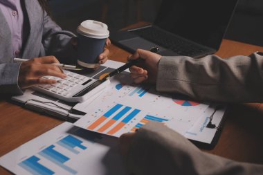 Group of confident business people point to graphs and charts to analyze market data, balance sheet, account, net profit to plan new sales strategies to increase production capacity.