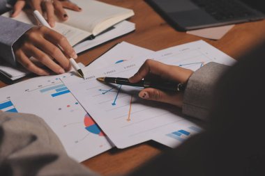 Group of confident business people point to graphs and charts to analyze market data, balance sheet, account, net profit to plan new sales strategies to increase production capacity.