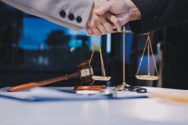 İki iş adamı bir hukuk bürosunda tartıyla ve masada tokmakla el sıkışıyor.