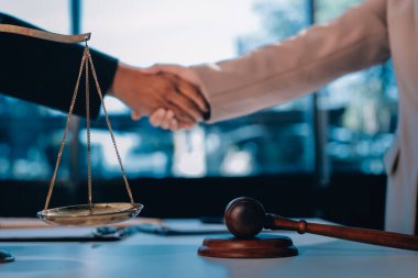 İki iş adamı bir hukuk bürosunda tartıyla ve masada tokmakla el sıkışıyor.