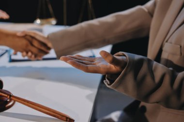 İki iş adamı bir hukuk bürosunda tartıyla ve masada tokmakla el sıkışıyor.