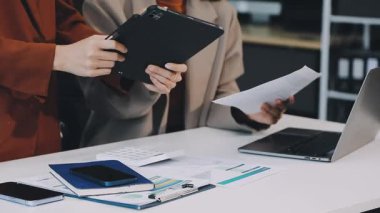 Modern ofiste çalışan genç bir kadın elinde tabletle belgelerini kontrol ediyor.