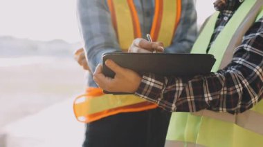 Sarı yelek giyen, elinde tablet olan ve inşaat alanında çalışan genç bir bayan işçi.