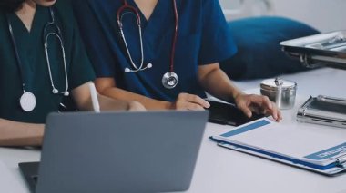 Masasında dizüstü bilgisayar ve tabletle oturan üniformalı genç bayan doktor..