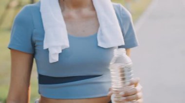 Spor kıyafetli genç kız parkta koştuktan sonra su içiyor.