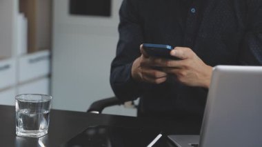 Adam akıllı telefon kullanıyor ve masada kahve içiyor.