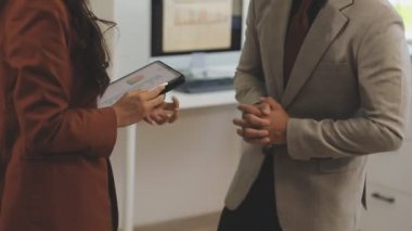 Takım elbiseli genç iş kadını ofiste iş arkadaşıyla tokalaşıyor.