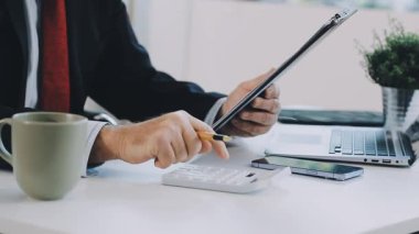 Ofiste hesap makineli dizüstü bilgisayar ve cep telefonu kullanan bir işadamı.