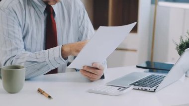 Takım elbiseli ve kravatlı işadamı elinde kalemle masaüstüne bir rapor yazıyor.
