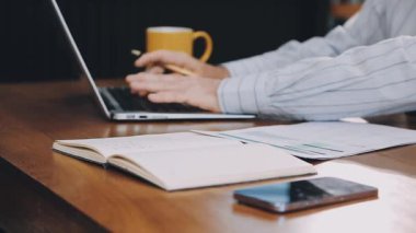 Beyaz gömlekli bir adam ev ofisinde çalışıyor, not defteri kullanıyor ve notlar yazıyor. Bir kafede cep telefonu ve laptop kullanan bir iş adamı.