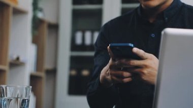 Yakın plan - dizüstü bilgisayarda yazarken akıllı telefon kullanan adam görüntüsü.