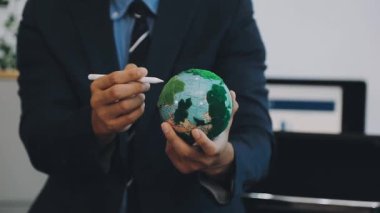 Yeşil bitkisi olan bir küreyi tutan iş adamı