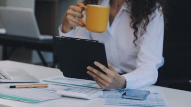 Bilgisayarda çalışan ve ofiste kahve içen genç bir kadın.