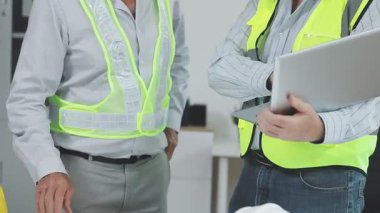 Güvenlik yeleği mühendisi elinde plan tutuyor ve konuşuyor.