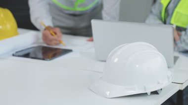 Dizüstü bilgisayarı ve miğferi olan mühendis ve mühendis plan üzerinde çalışıyorlar.