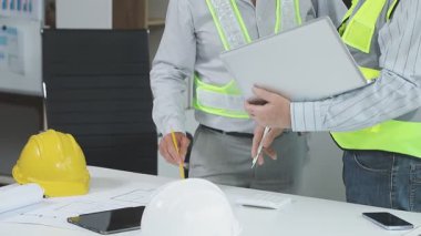 Sarı takım elbiseli ve miğferli erkek işçi iş yerinin planlarını tutuyor.